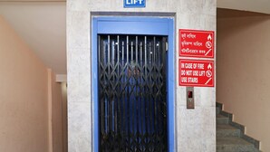 A lift door with a blue frame and a metal security gate, accompanied by a fire safety sign and a lift control panel. - OYO 4979 Prabha Palace Lodge (Guwahati)
