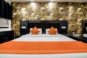 A hotel room with a large bed, two orange pillows, a black headboard, and a wall with a detailed mural.