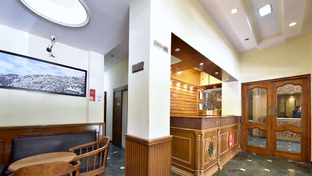 Un espace d’accueil avec un comptoir de réception en bois, un coin salon avec des chaises, une caméra de surveillance fixée au mur et une vue sur un paysage enneigé.