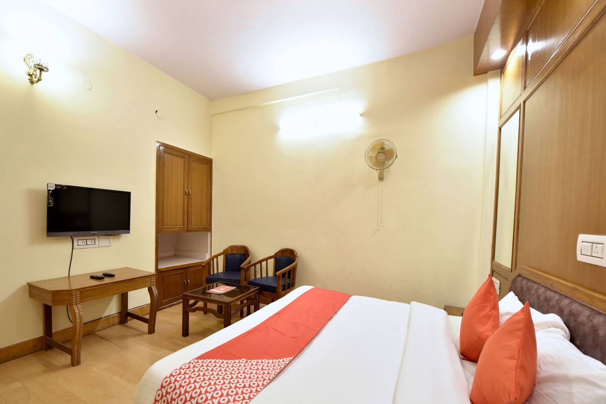 Habitación de hotel con cama, escritorio, televisor y armario.