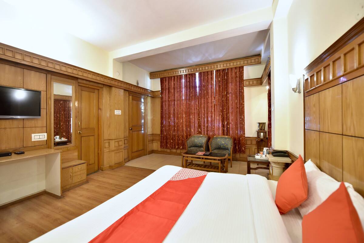 Habitación de hotel con una cama grande, armario de madera, televisión, escritorio y dos sillas.