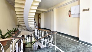Un hall d’hôtel moderne avec un escalier en marbre, des plantes en pot et un extincteur fixé au mur.