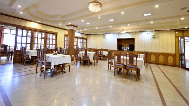 Une salle de banquet spacieuse, dotée de nombreuses tables et chaises, d’un lustre et de grandes fenêtres laissant entrer la lumière naturelle.