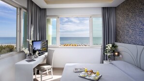 Habitación de hotel con escritorio, cama, televisión y vista a la playa.