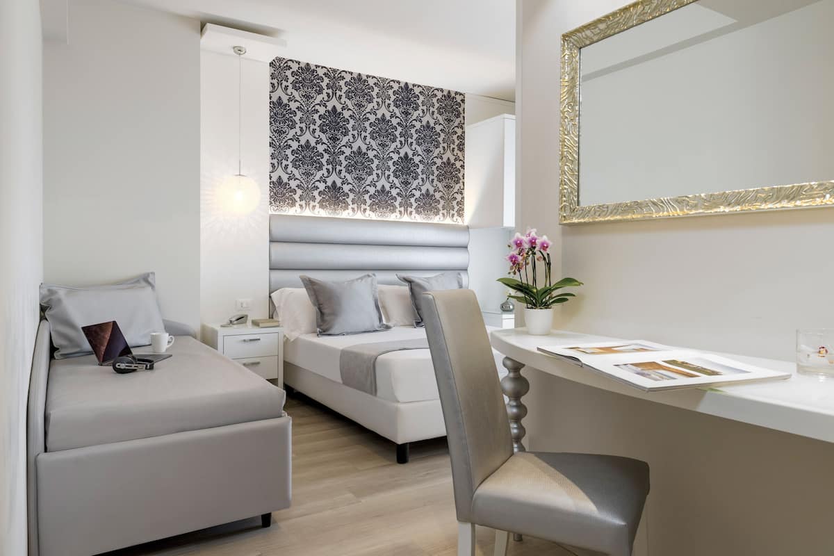 A modern bedroom with a bed, bedside table, lamp, and a desk with a chair.