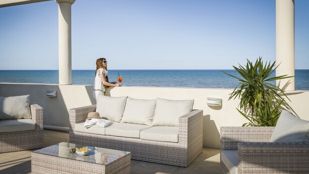 Un espacio al aire libre cubierto con mobiliario de mimbre, una mesa de vidrio y vista al mar.
