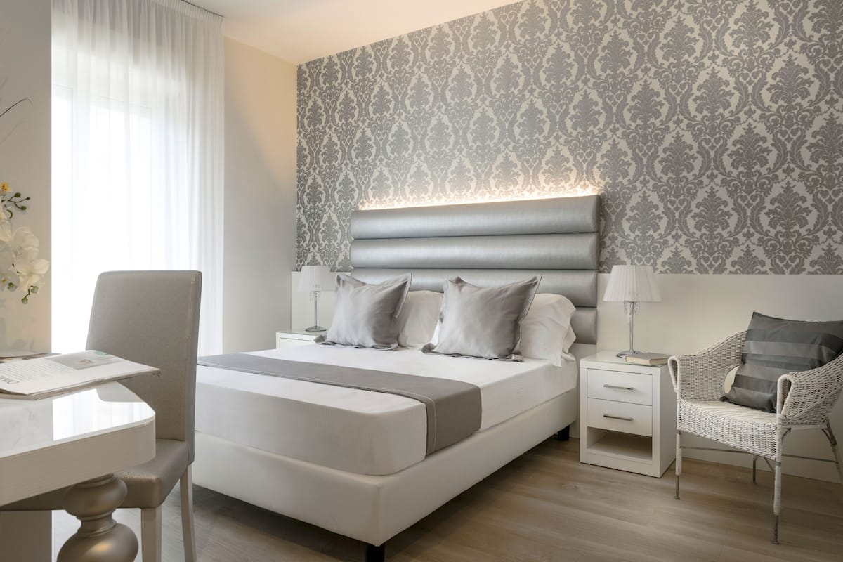 A modern hotel room with a large bed, bedside tables, a chair, and a desk.
