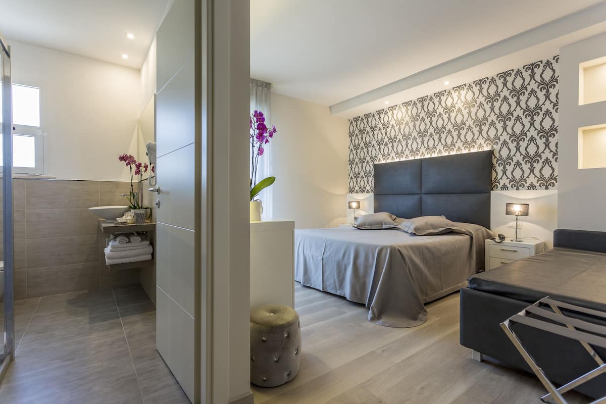 A modern bedroom with a large bed, bedside tables, a nightstand, and a small seating area.