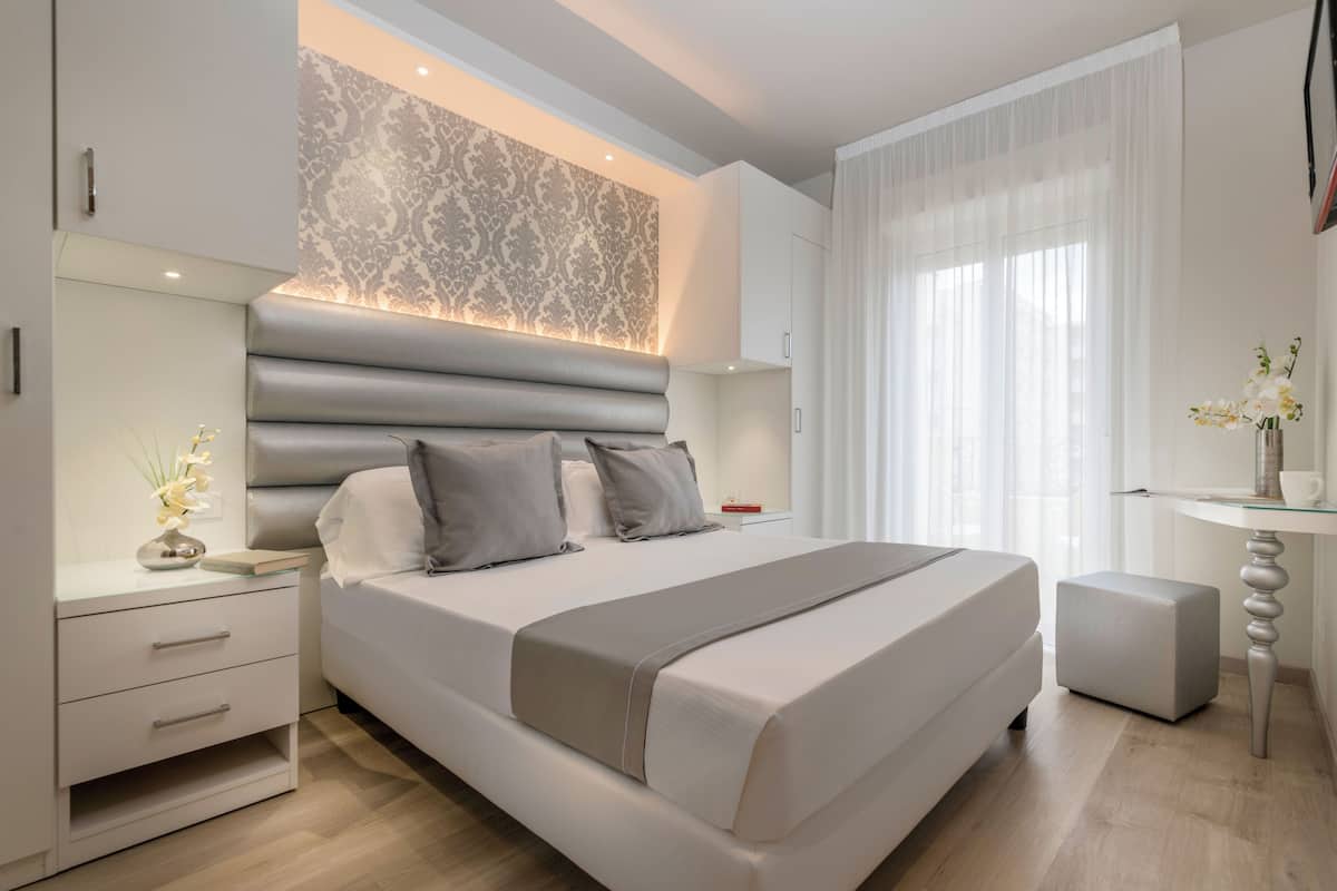 A modern bedroom with a large bed, bedside tables, a nightstand, a decorative wall, and a window with curtains.