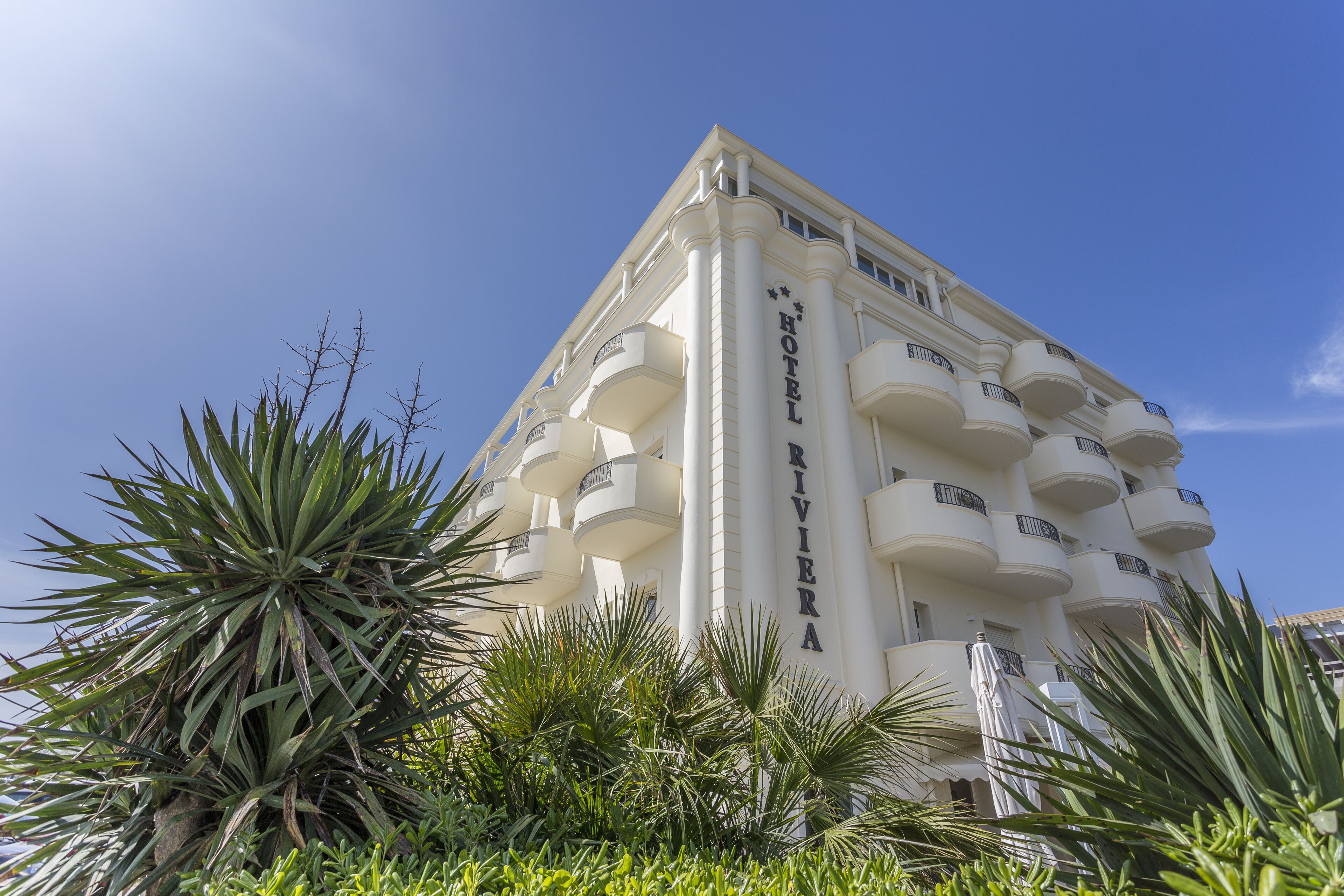 Un hôtel blanc doté de balcons, sous un ciel d’un bleu limpide.