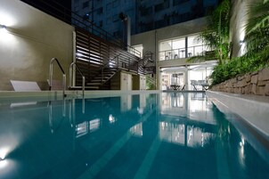 Una piscina interior con una escalera, un muro de piedra y vistas a un edificio con amplias ventanas.