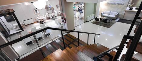 A modern hotel interior with a glass staircase, a reception area, and a lounge with a sofa.