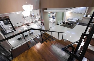 Un interior de hotel moderno con una escalera de cristal, una zona de recepción y un salón con sofá.