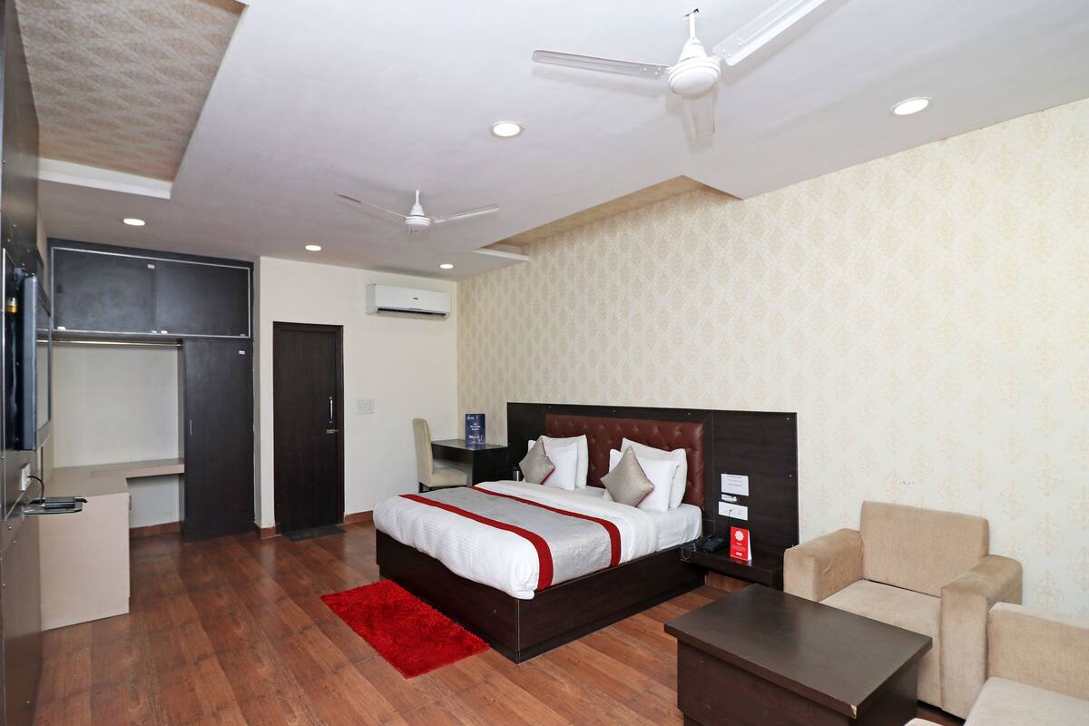 Quarto de hotel com uma cama grande, uma escrivaninha, uma cadeira, um sofá, um tapete vermelho e um ventilador de teto.