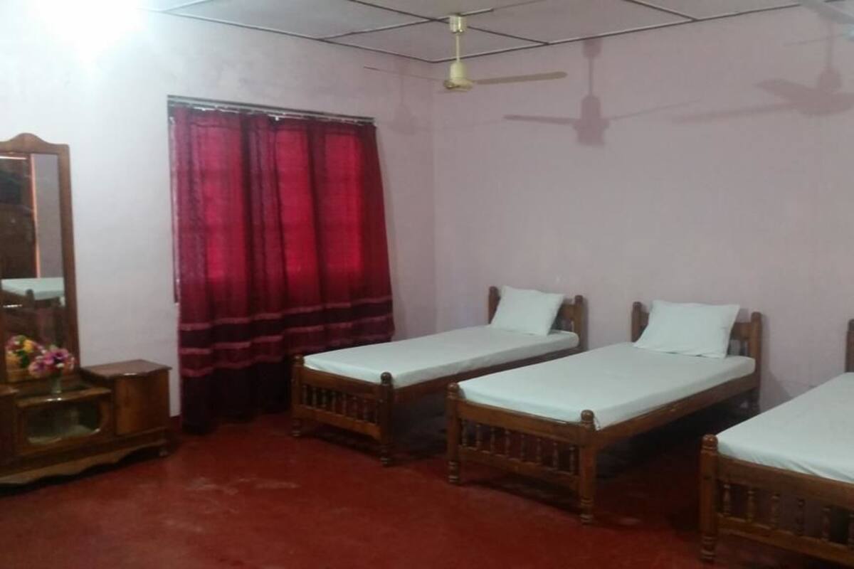 Una habitación con tres camas individuales, un armario de madera, un espejo y una cortina roja.