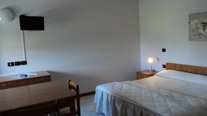 A bedroom with a bed, bedside table, lamp, desk, chair, and a television mounted on the wall. - Hotel Cinzia (Savignano sul Panaro)