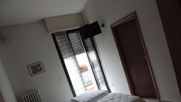 Een slaapkamer met een bed, een radiator, een raam met zonwering en een deur.