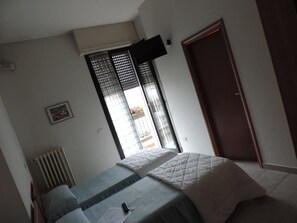 Une chambre à coucher avec un lit, un radiateur, une fenêtre avec des stores et une porte.