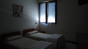 A dimly lit room with two single beds, a small bedside table, and a window with sheer curtains. - Hotel Cinzia (Savignano sul Panaro)