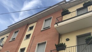 Een meerhoog gebouw met een bakstenen gevel, meerdere balkons met zwarte hekwerken, en een heldere lucht op de achtergrond.
