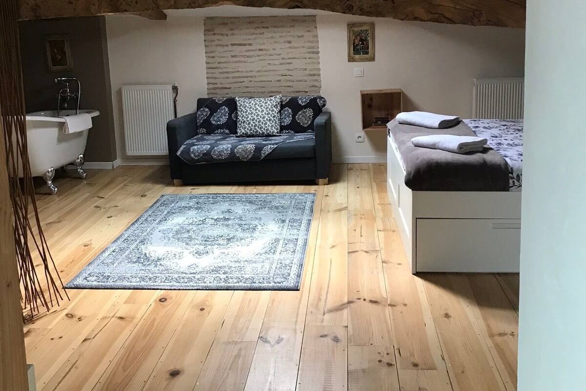 A room with wooden beams, a sofa, a bed, a radiator, and a bathtub.