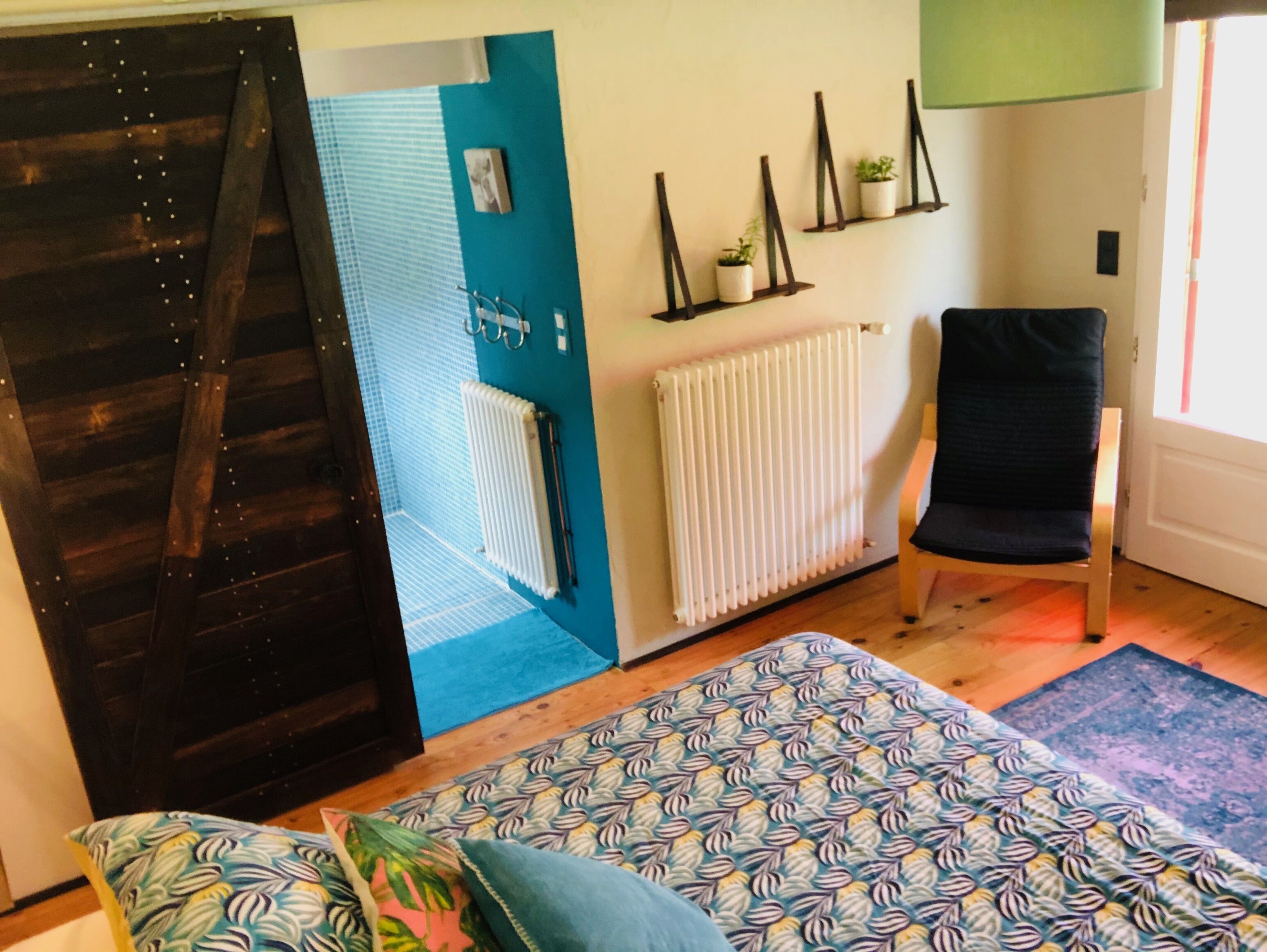 Una habitación con una cama, una silla, un radiador y una pared con estanterías que albergan plantas.