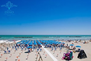 Een strand met rijen blauwe en witte ligbedden en parasols, een heldere lucht en de oceaan op de achtergrond.