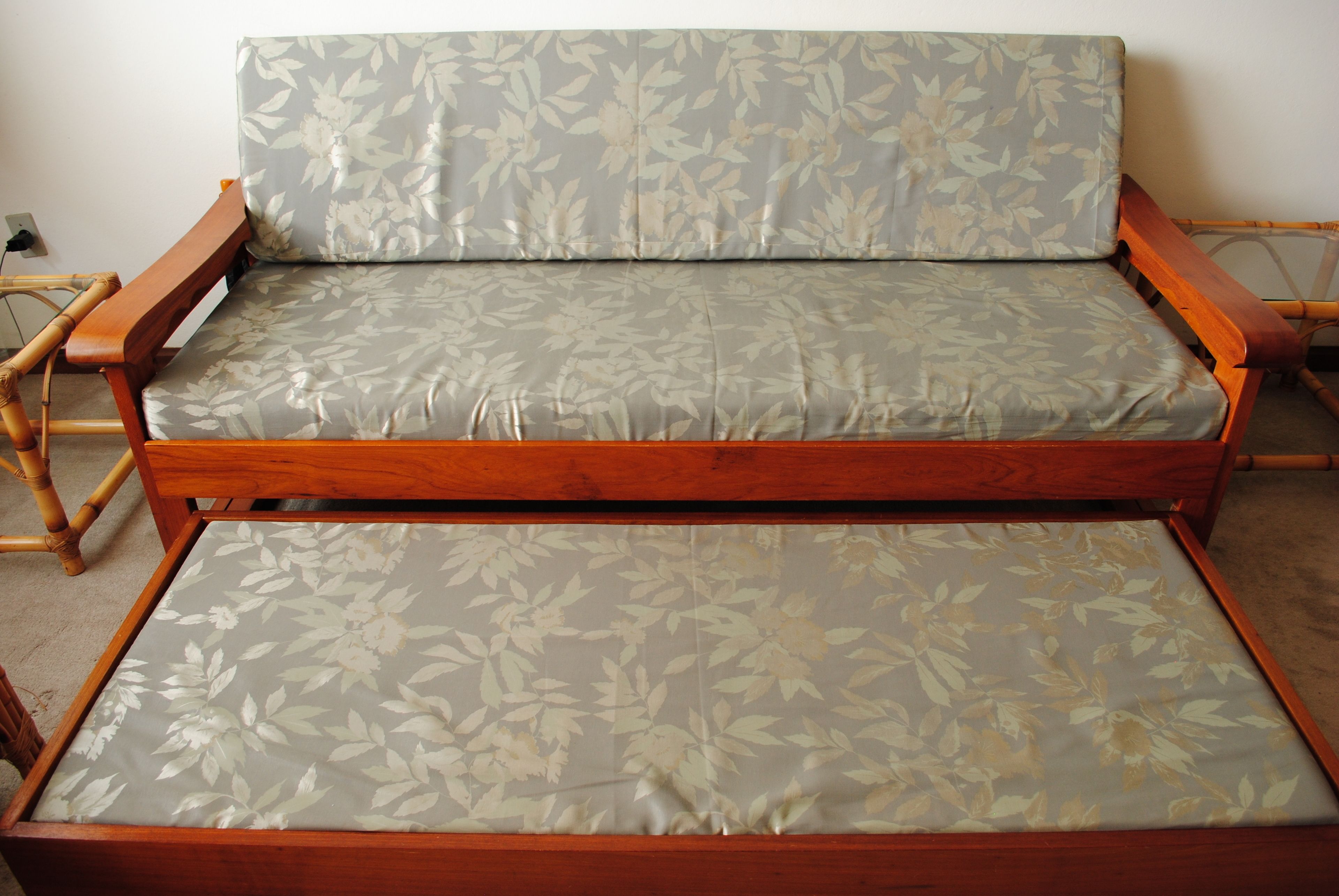 A wooden sofa with a floral fabric cushion in a room with a plain wall and a power outlet.