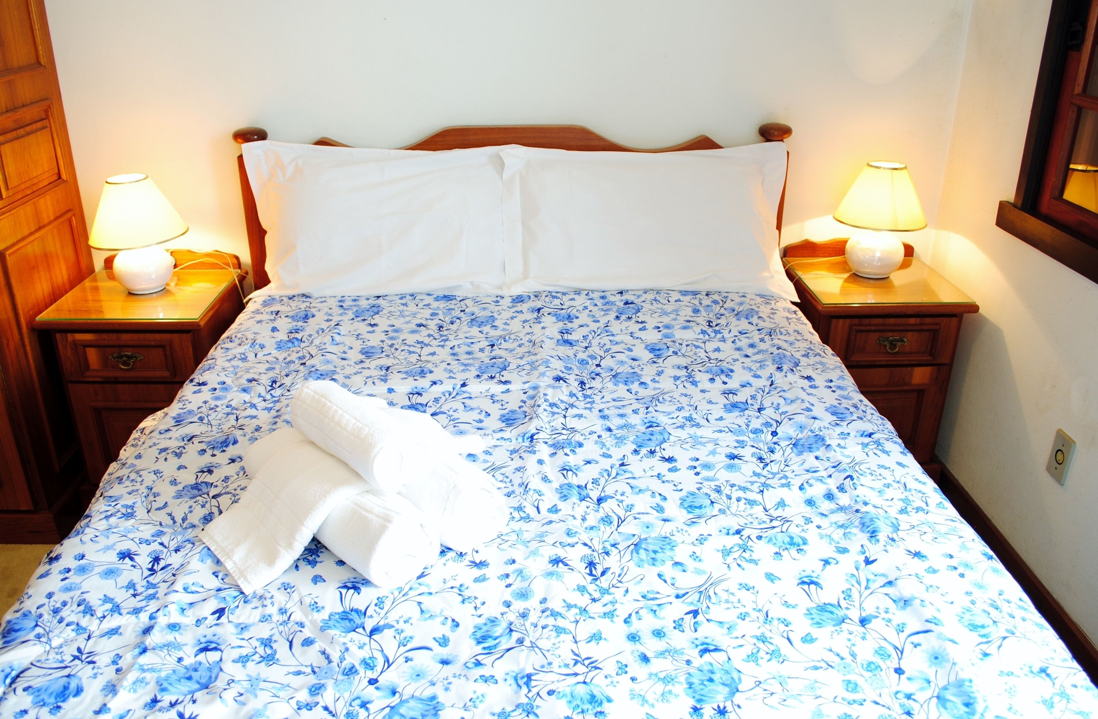 A bed with a floral bedspread, two bedside lamps, and a folded towel on the bed.