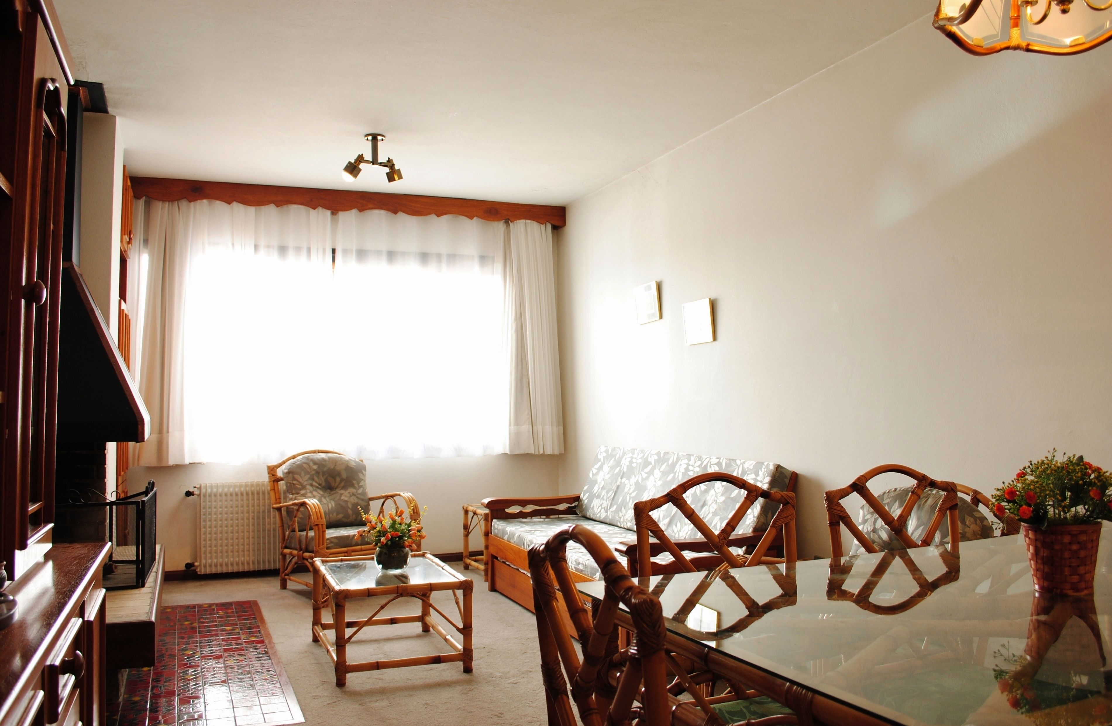A cozy living room with a sofa, chairs, a glass dining table, and a large window with curtains.
