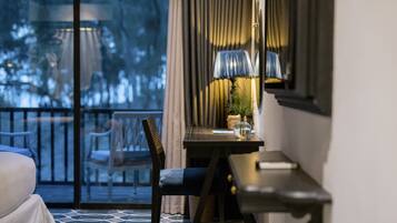 A hotel room with a bed, a desk with a lamp, a chair, and a view of the outdoors through a glass door.