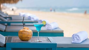 A beachside lounge with a coconut drink and a blue cocktail on a table, overlooking the ocean.