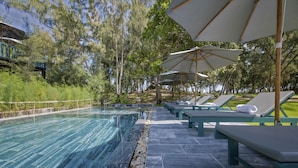 A pool area with lounge chairs and umbrellas, surrounded by trees.