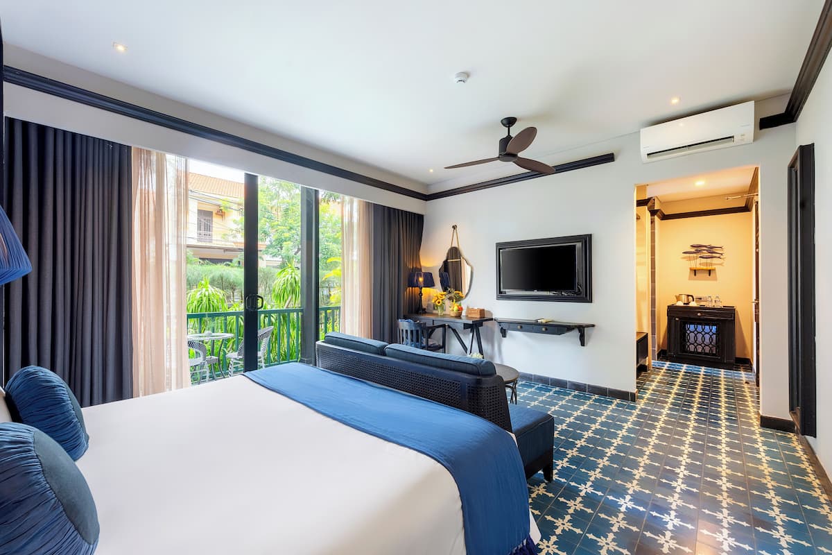 Habitación de hotel con una cama grande, un escritorio con una silla, un televisor y un balcón con cortinas.