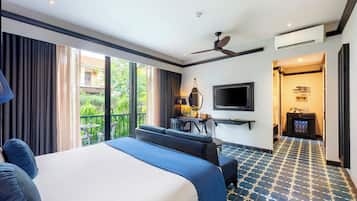 A hotel room with a large bed, a desk with a chair, a TV, and a balcony with curtains.