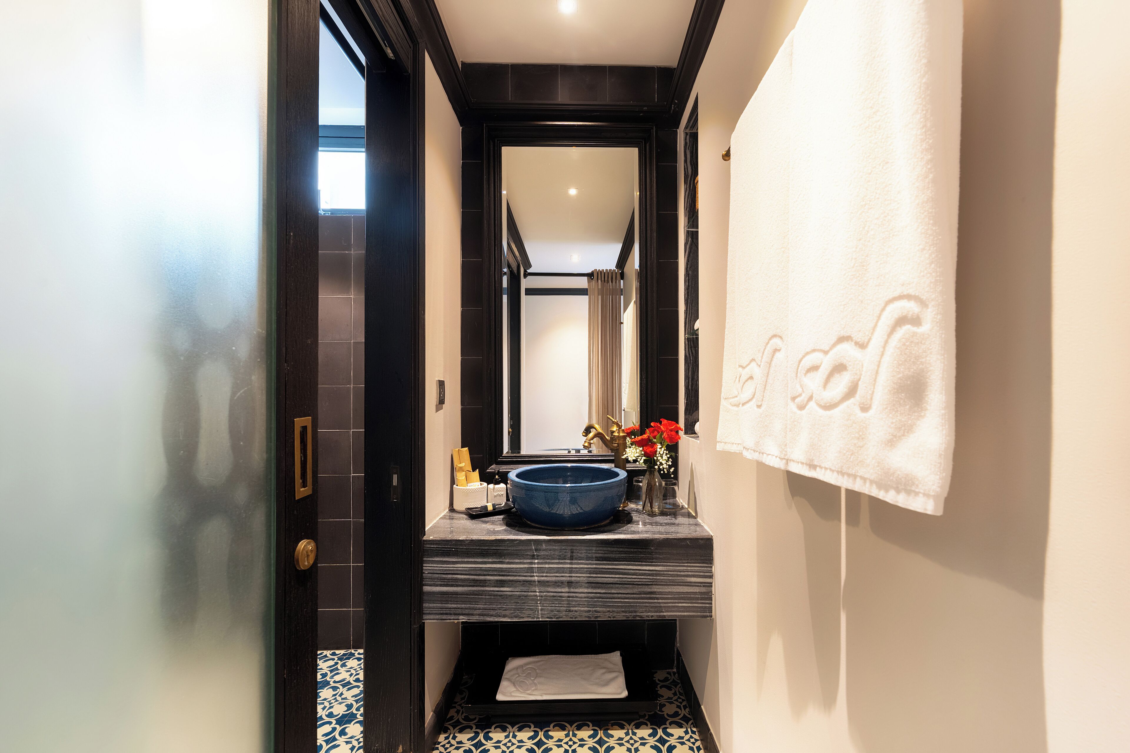 Une petite salle de bain avec un sol carrelé foncé, un lavabo bleu et une serviette blanche accrochée au mur.