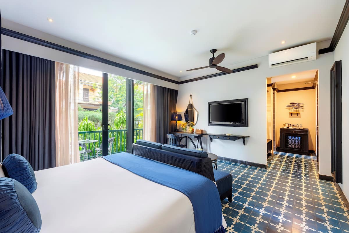 Habitación de hotel con cama, escritorio, televisor y balcón con vistas a zonas verdes.