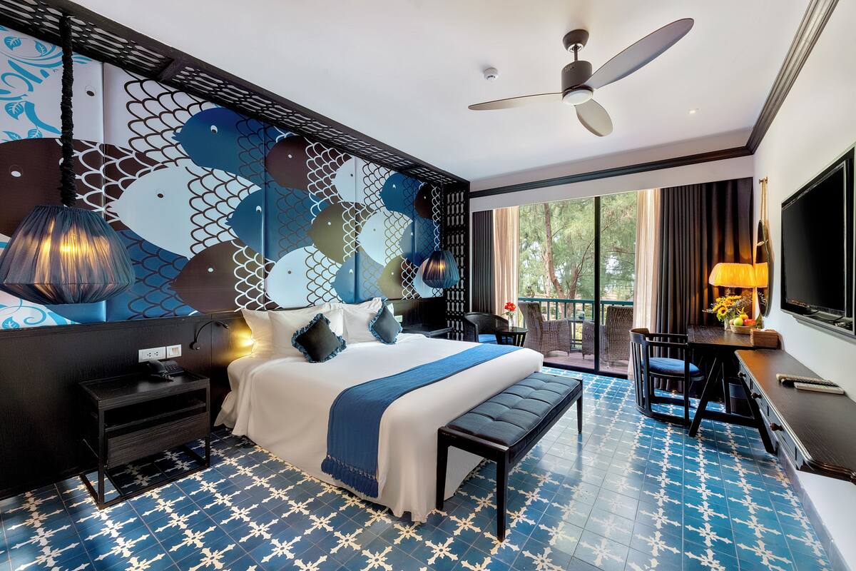 Habitación de hotel moderna con una cama grande, un escritorio, una silla, un banco y un televisor.