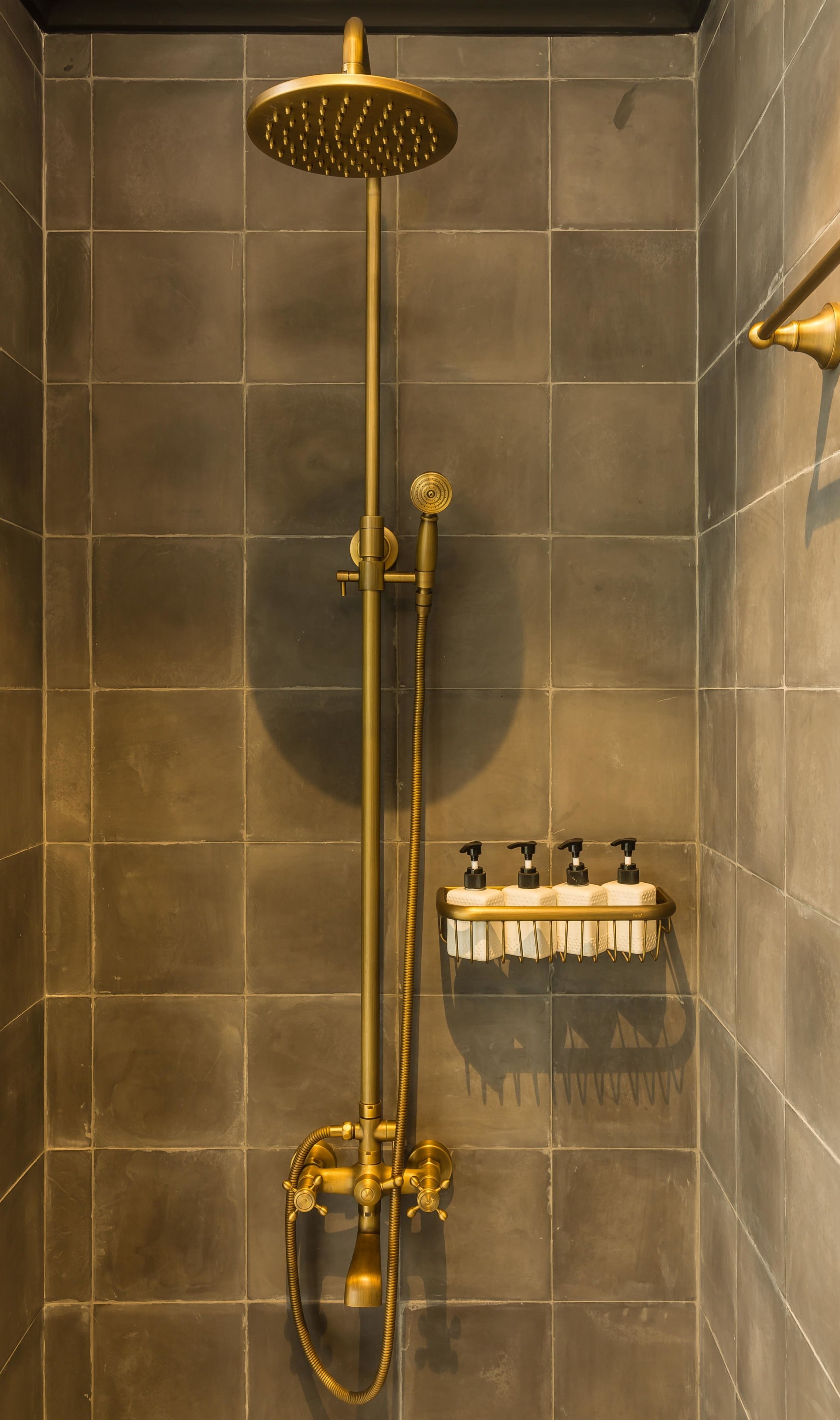 A shower with a golden showerhead and hose, a towel rack with towels, and a wall-mounted faucet.
