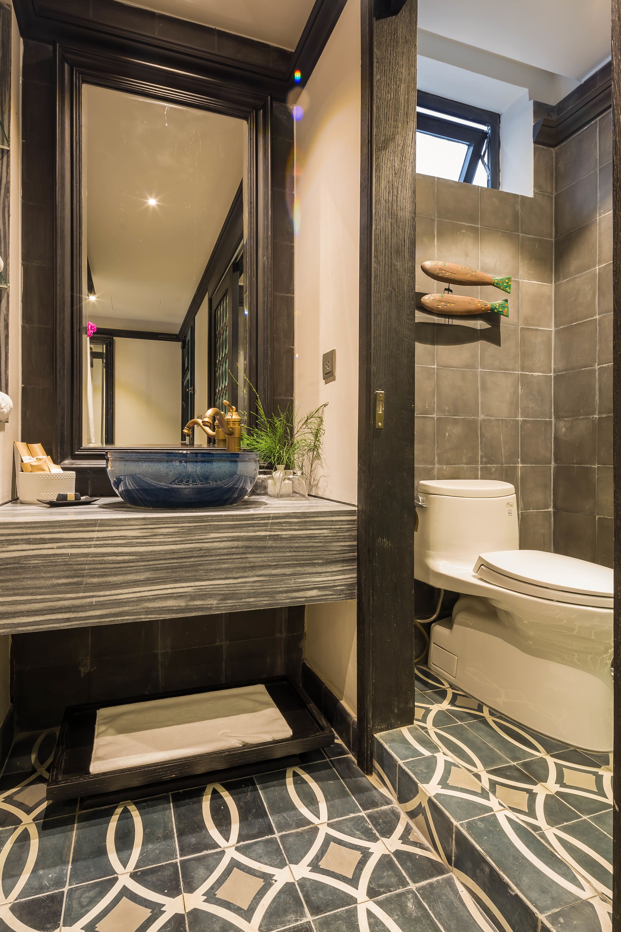 Une salle de bain avec un grand miroir, un lavabo en céramique bleue, des toilettes blanches et un carrelage décoré.