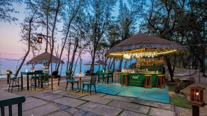 An outdoor bar area with thatched umbrellas, seating, and a view of the sea.