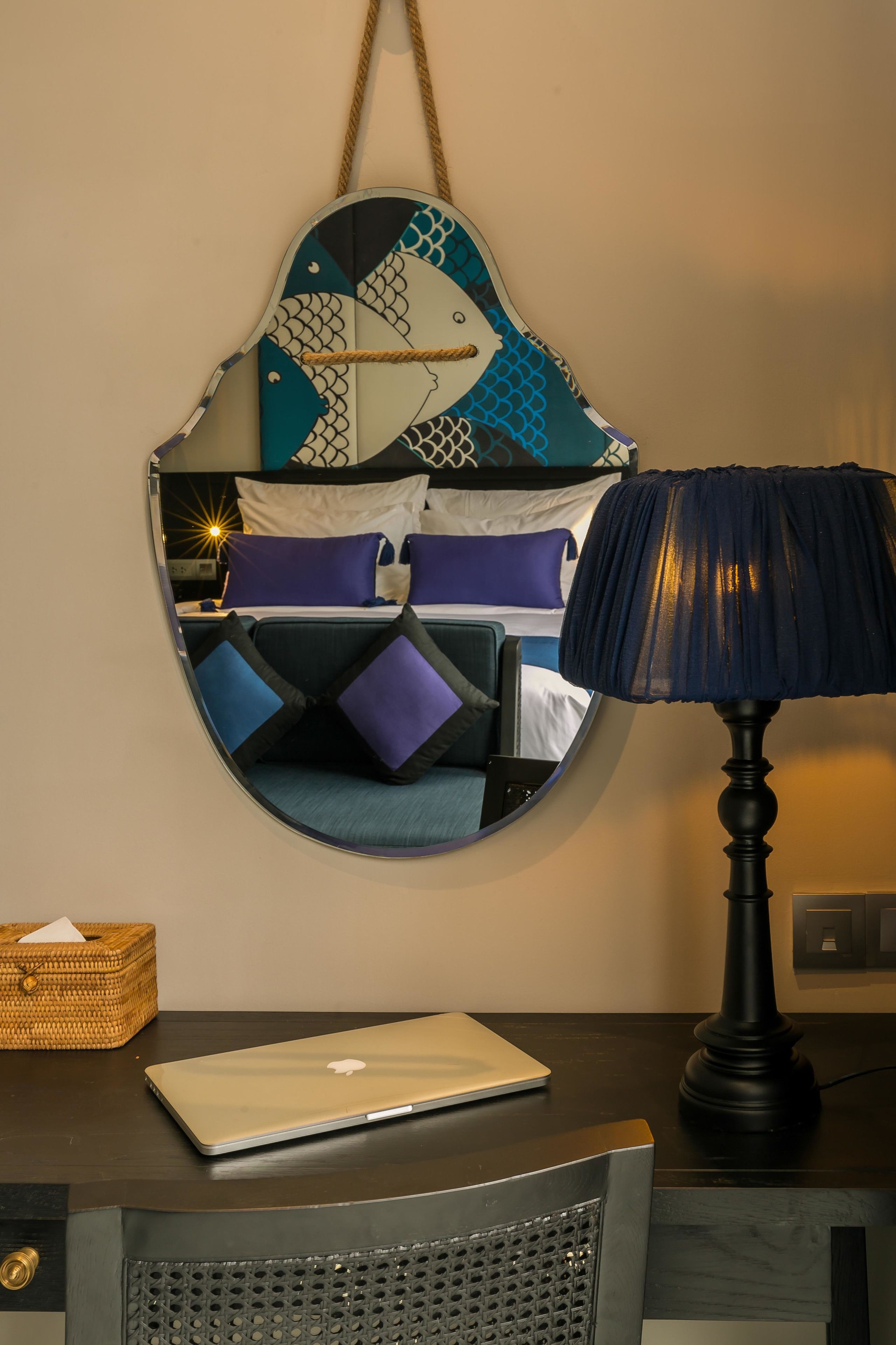 Una cama con un cabecero estampado en azul y blanco, una laptop sobre una mesita de noche, una lámpara azul oscuro y una cesta de mimbre.