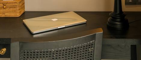 Una cama con un cabecero estampado en azul y blanco, una laptop sobre una mesita de noche, una lámpara azul oscuro y una cesta de mimbre.
