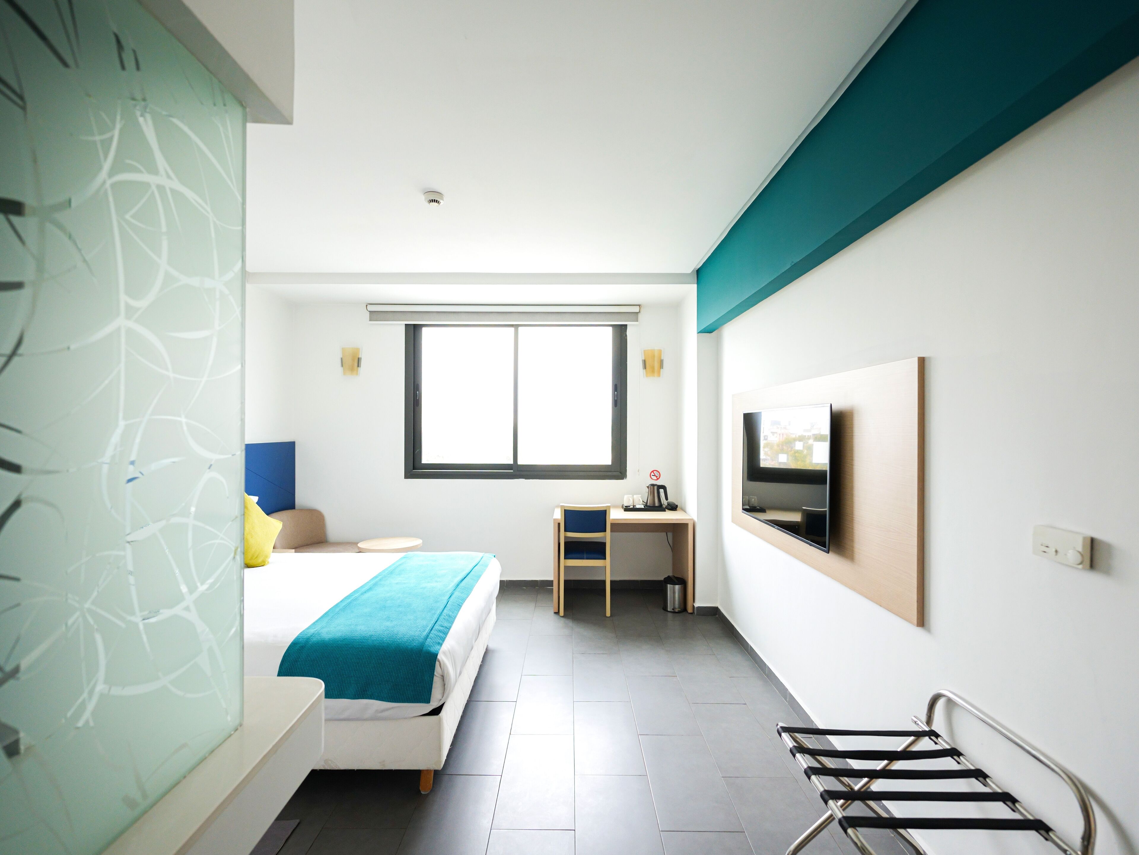 Una habitación de hotel moderna con cama, escritorio, televisor y ventana.