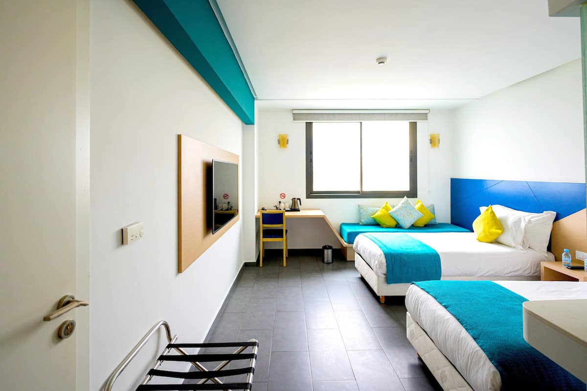 A hotel room with two beds, a desk, a chair, a TV mounted on the wall, and a window.