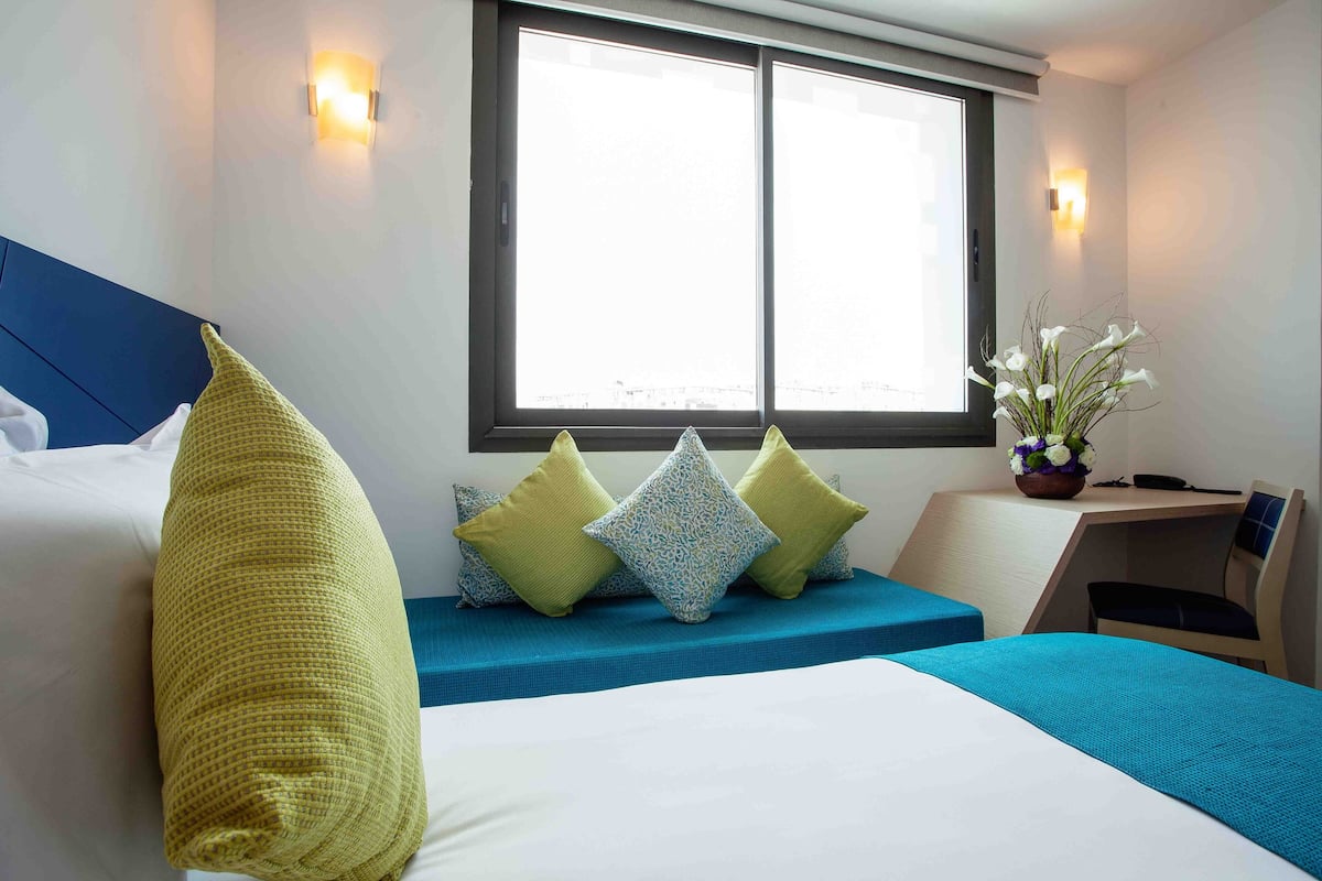 A hotel room with a bed, a desk, and a window.