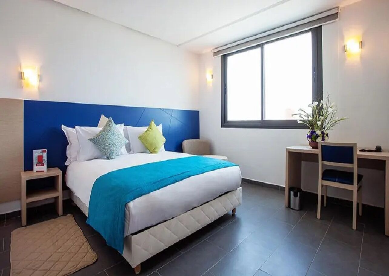Ein modernes Hotelzimmer mit einem großen Bett, einem Schreibtisch, einem Sessel und einem Fenster.
