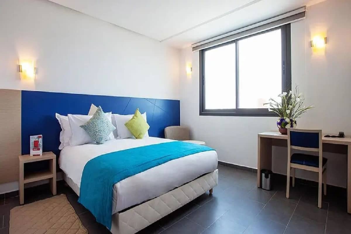 A modern hotel room with a large bed, a desk, and a window.