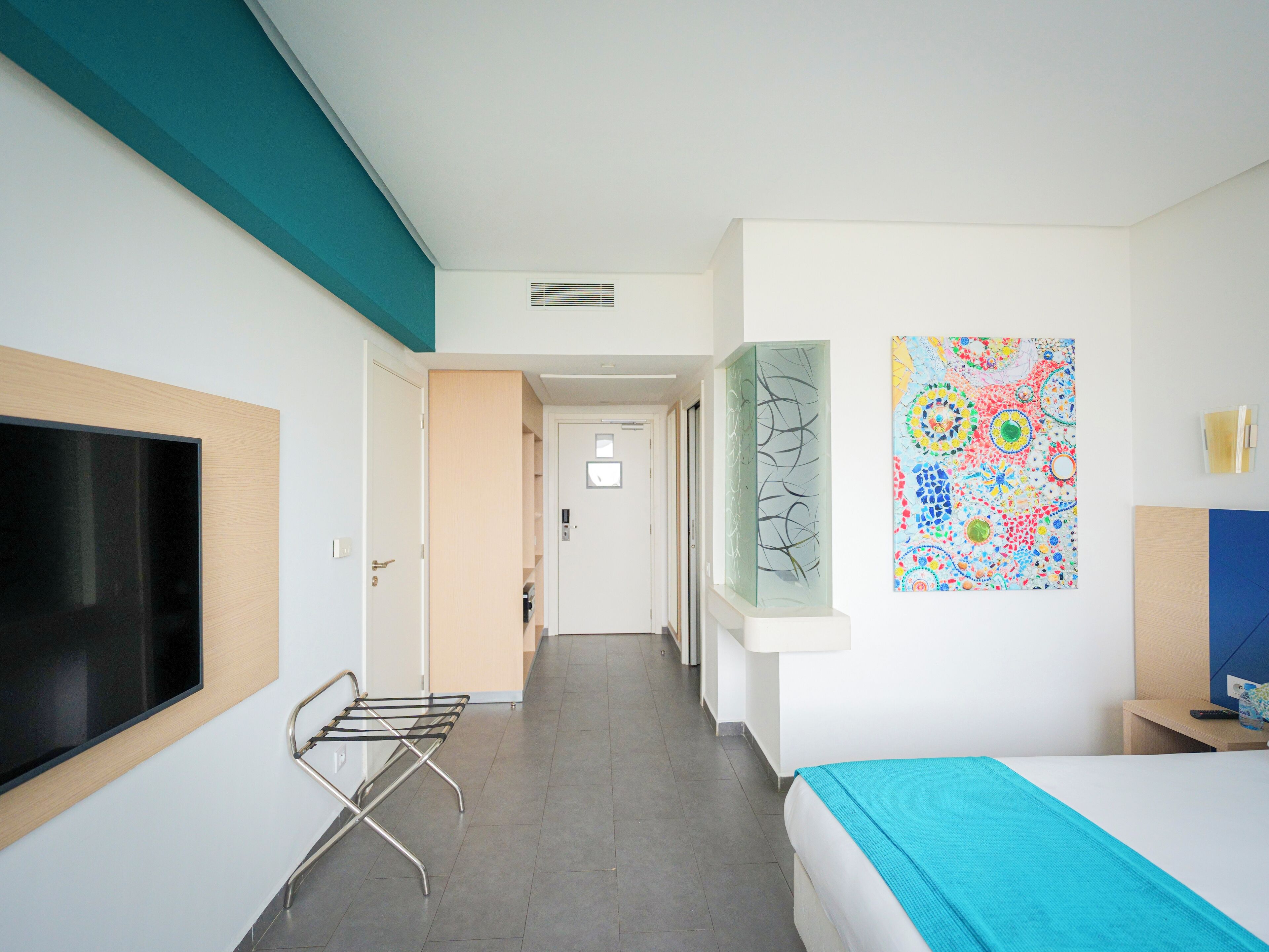 Un couloir d’hôtel avec un lit, une télévision et une œuvre d’art murale.