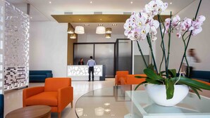 A modern lobby with orange seating, a reception desk, and a large orchid plant.